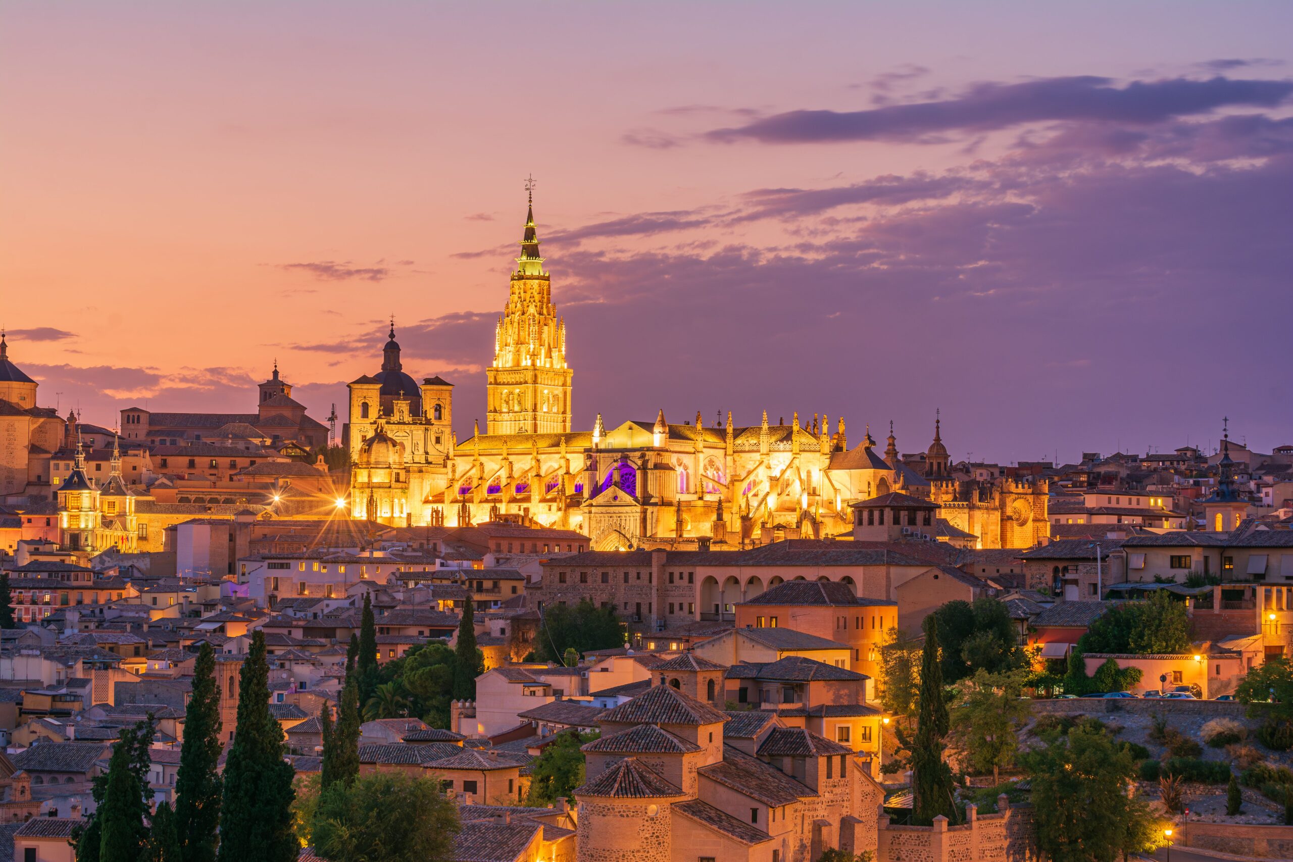 A stunning view of Toledo's skyline at sunset, highlighting the illuminated cathedral and historic architecture.